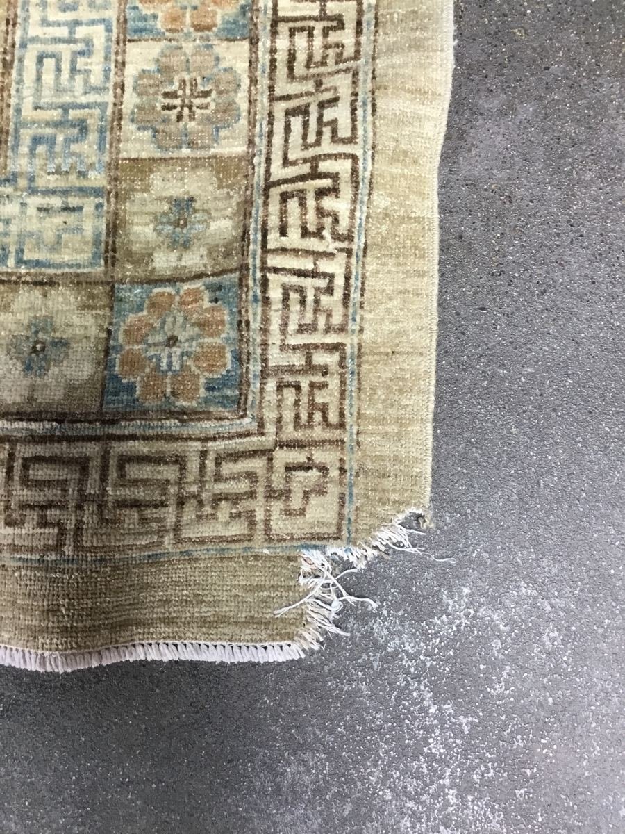 A Khotan rug with a chewed corner — frayed fringe and damage to the foundation