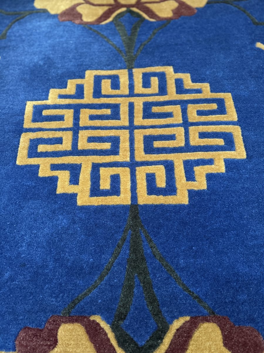 Classic Tibetan rug with golden geometric knot pattern on deep blue ground with floral motifs