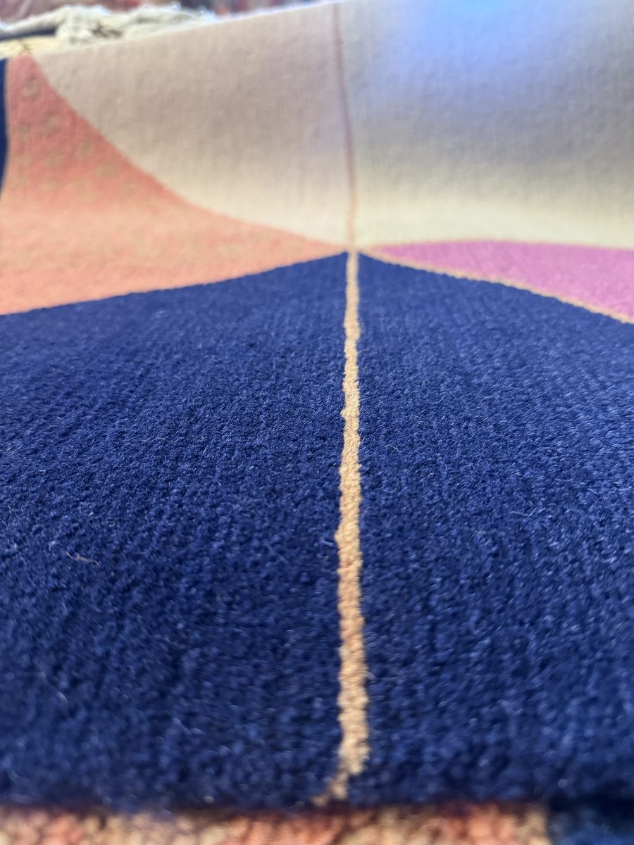 Close-up of fine 100-knot Nepali rug showing dense navy pile with geometric color blocks in rose and blue